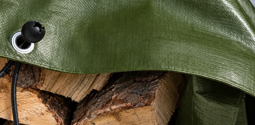 Planen-Fachhandel-Qualität von Koppi Kunststoffe: So lagert Ihr Kaminholz dauerhaft trocken, sicher geschützt vor Wind und Wetter. Dunkelgrüne Holzabdeckplane mit Kugelspanner auf gestapeltem Brennholz.
